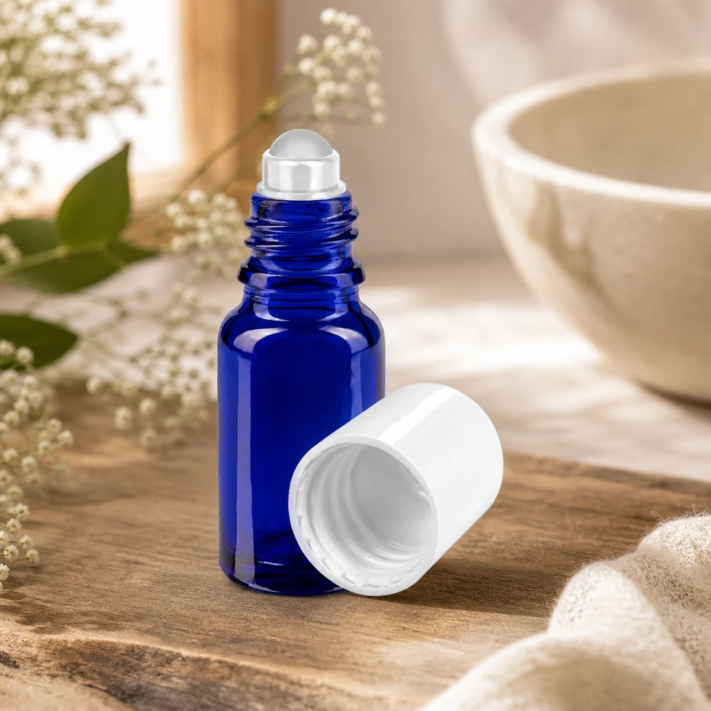 Flacone roll-on 10ml blu STD bianco ApoGlas Flacone di vetro roll-on da 10 ml, di colore blu cobalto, aperto, con il tappo bianco rimosso, su fondo di legno