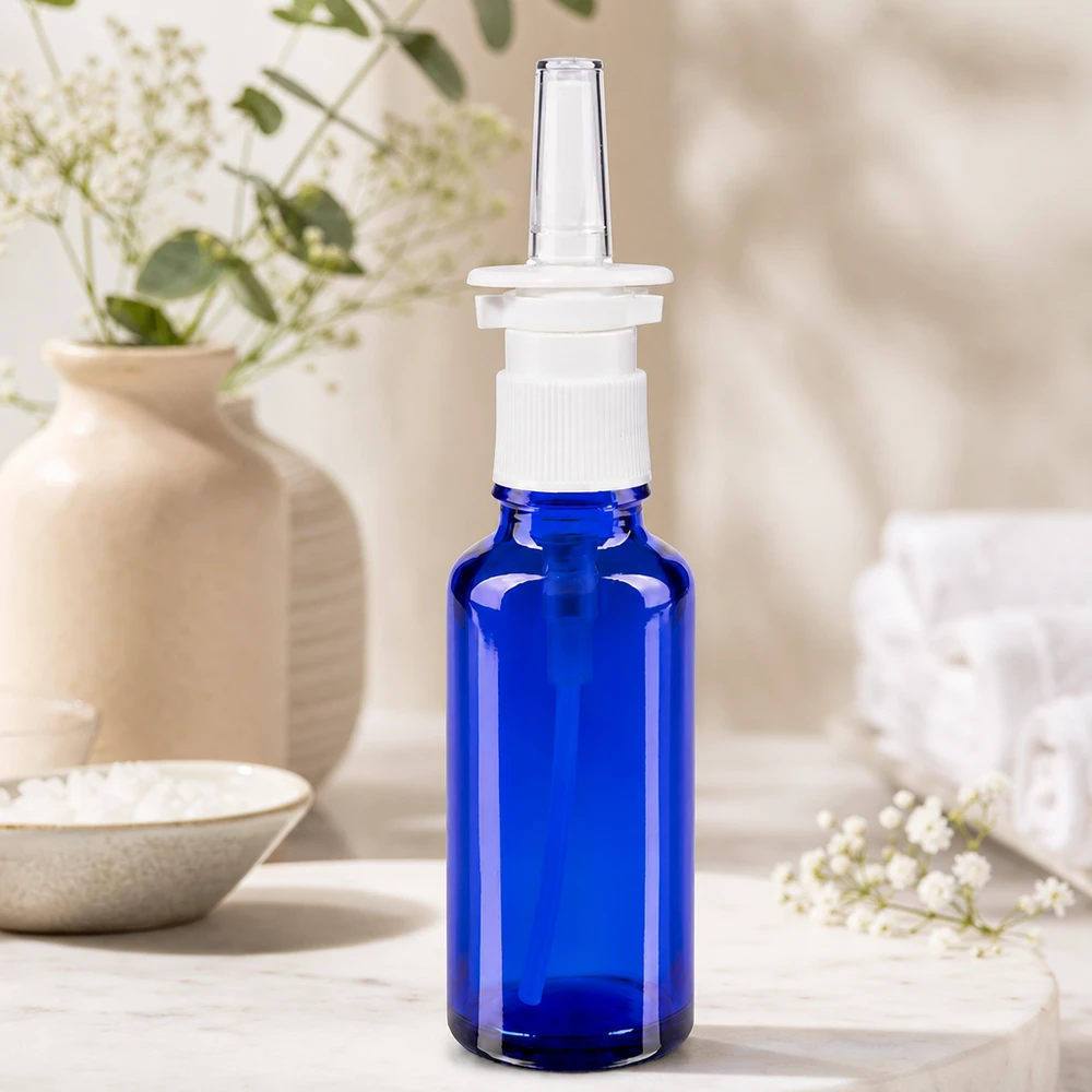 Seitenansicht blaue Pharmaflasche 30ml mit weißem Nasalsprayer auf hellem Marmoruntergrund