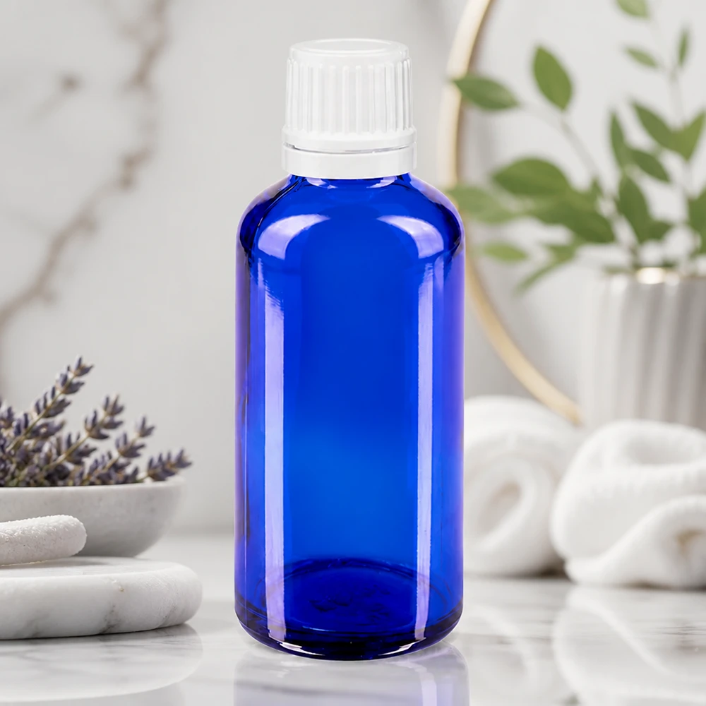 Bouteille en verre bleue de 50 ml avec un bouchon à vis blanc, posée sur du marbre à côté de la lavande