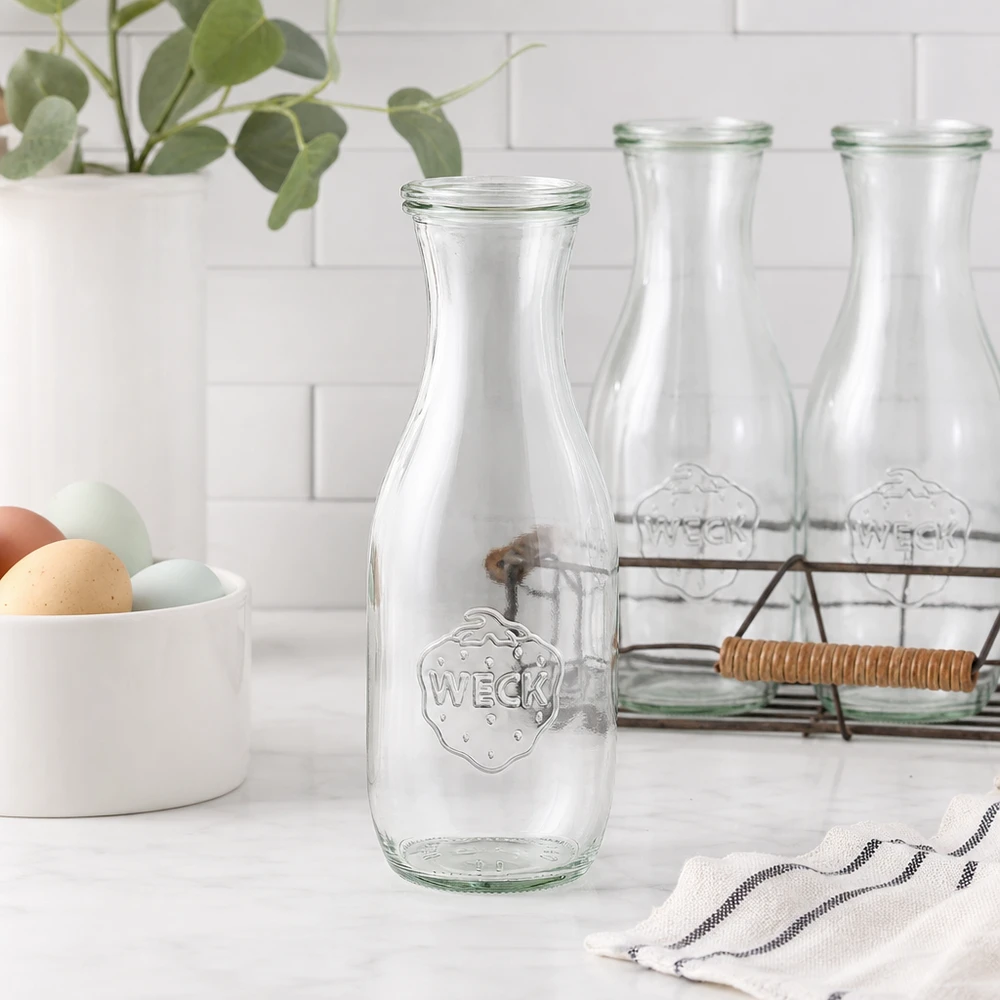 Bouteille à jus de 1 062 ml avec couvercle en verre WECK RR60 WECK Saftflasche 1062ml Glasflasche leer in moderner weißer Küche mit Eierschale Drahtkorb und Pflanze