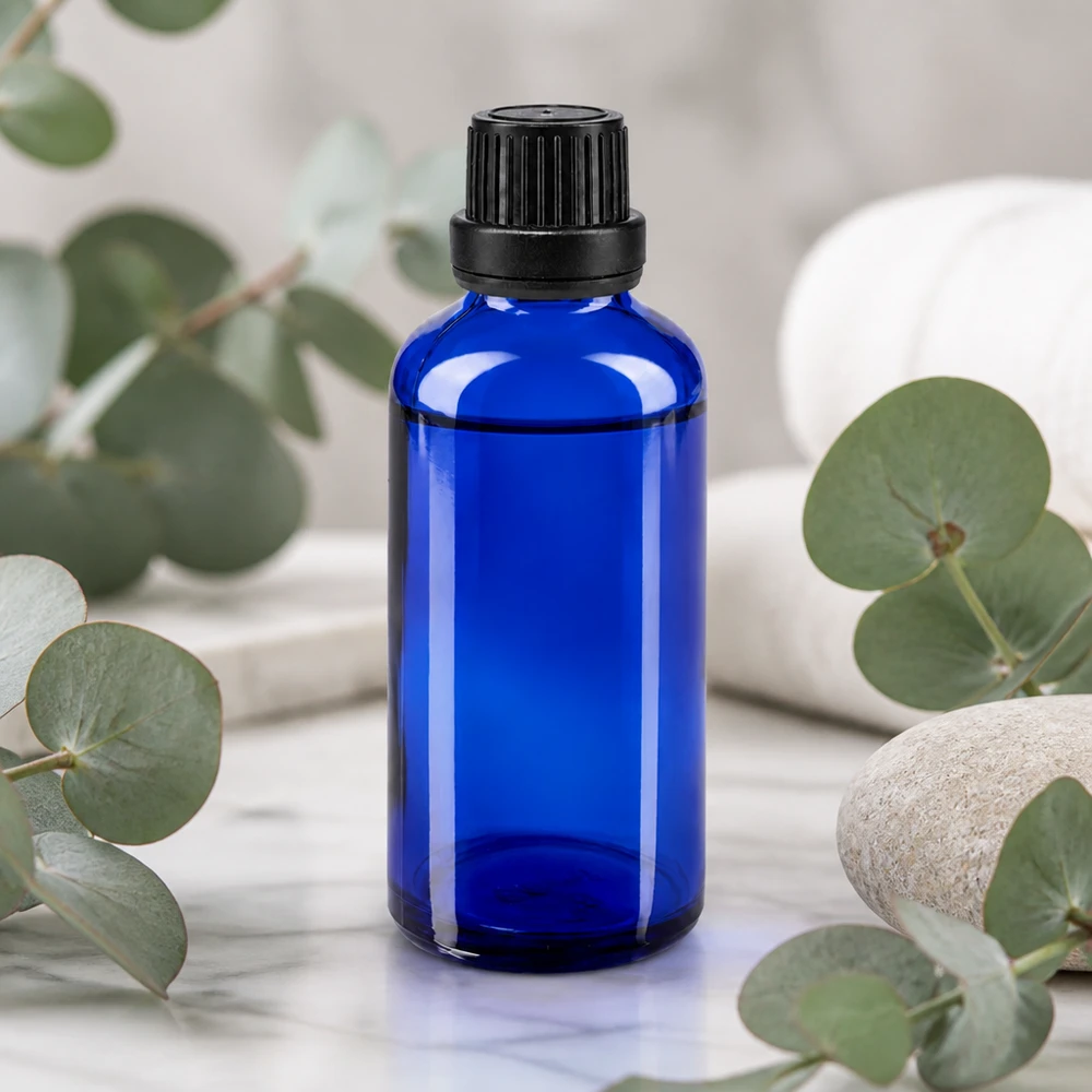Flacon en verre de pharmacie bleu cobalt de 50 ml, muni d'un bouchon de sécurité noir pour enfants, devant des branches d'eucalyptus
