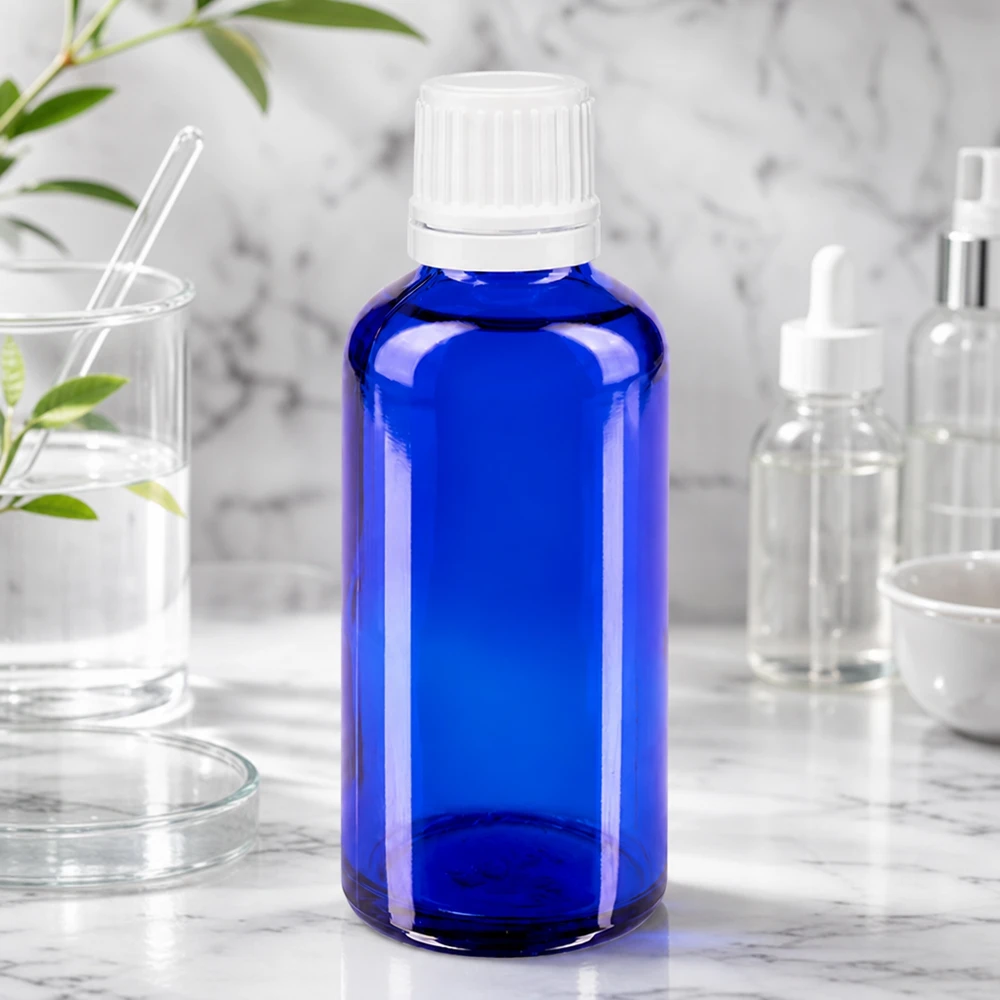 Petite bouteille en verre bleue avec un bouchon compte-gouttes, posée sur du marbre et entourée d'ustensiles de laboratoire et de plantes