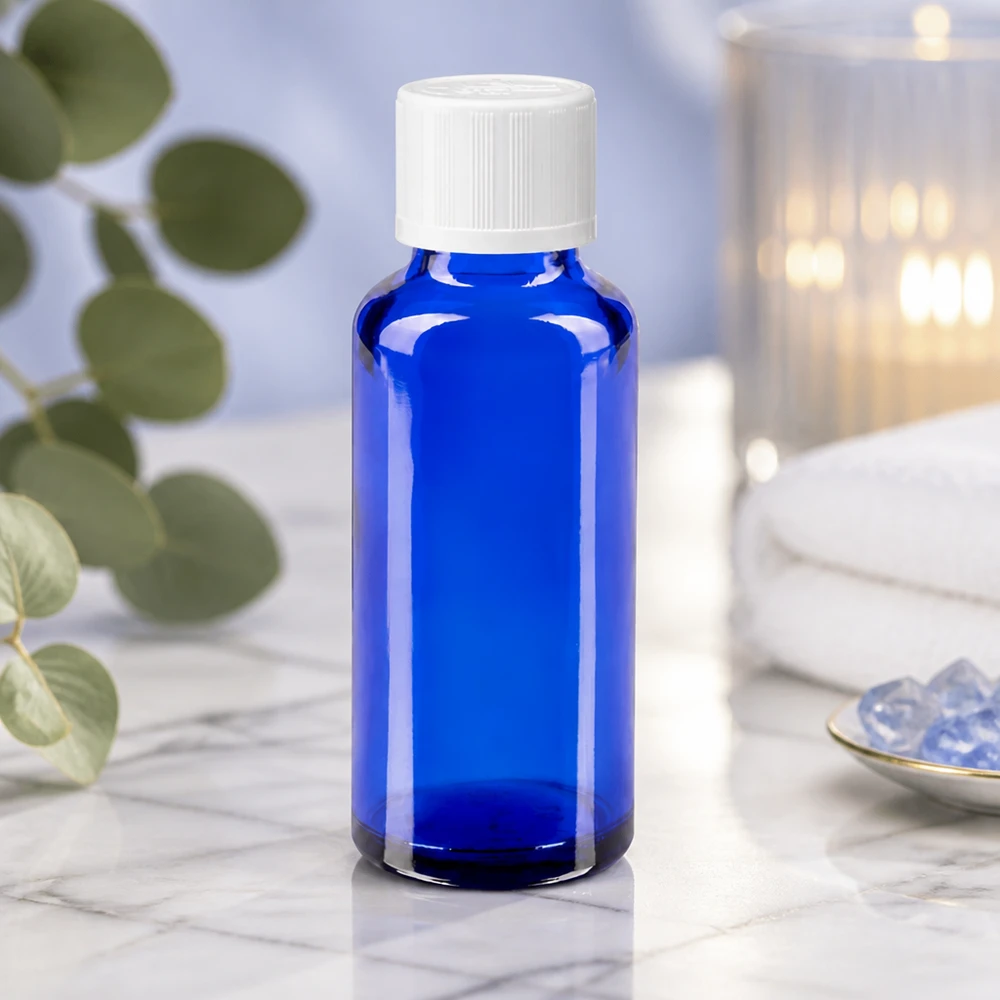 Contagocce blu da 30 ml. STD KiSi bianco/1,2mm ApoGlas Vaso da farmacia blu da 30 ml con tappo a vite bianco su un piano di marmo bianco, accanto a cristalli e una candela