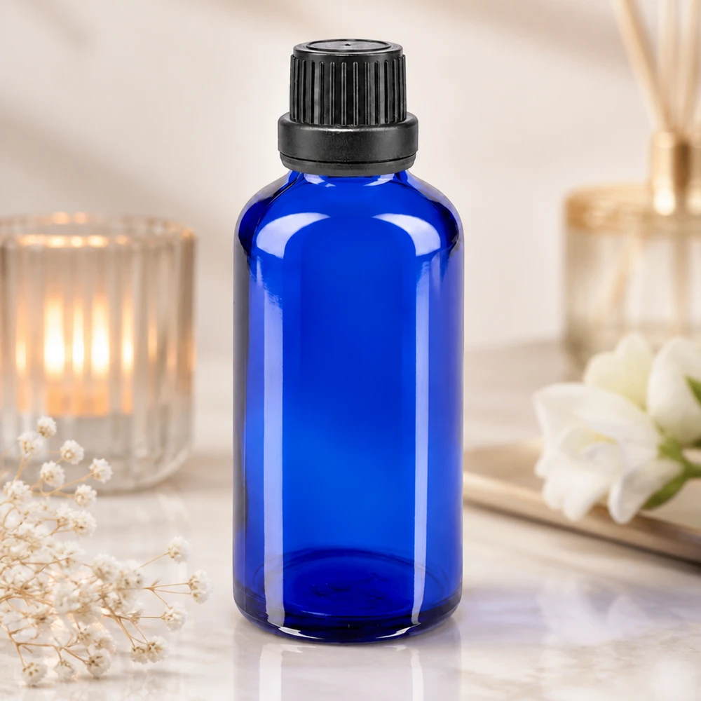 Flacon à pharmacie bleu 50ml bouchon inviolabilité 2mm noir Flacon en verre bleu cobalt de 50 ml avec bouchon à vis noir et compte-gouttes, à côté d'une bougie et de fleurs