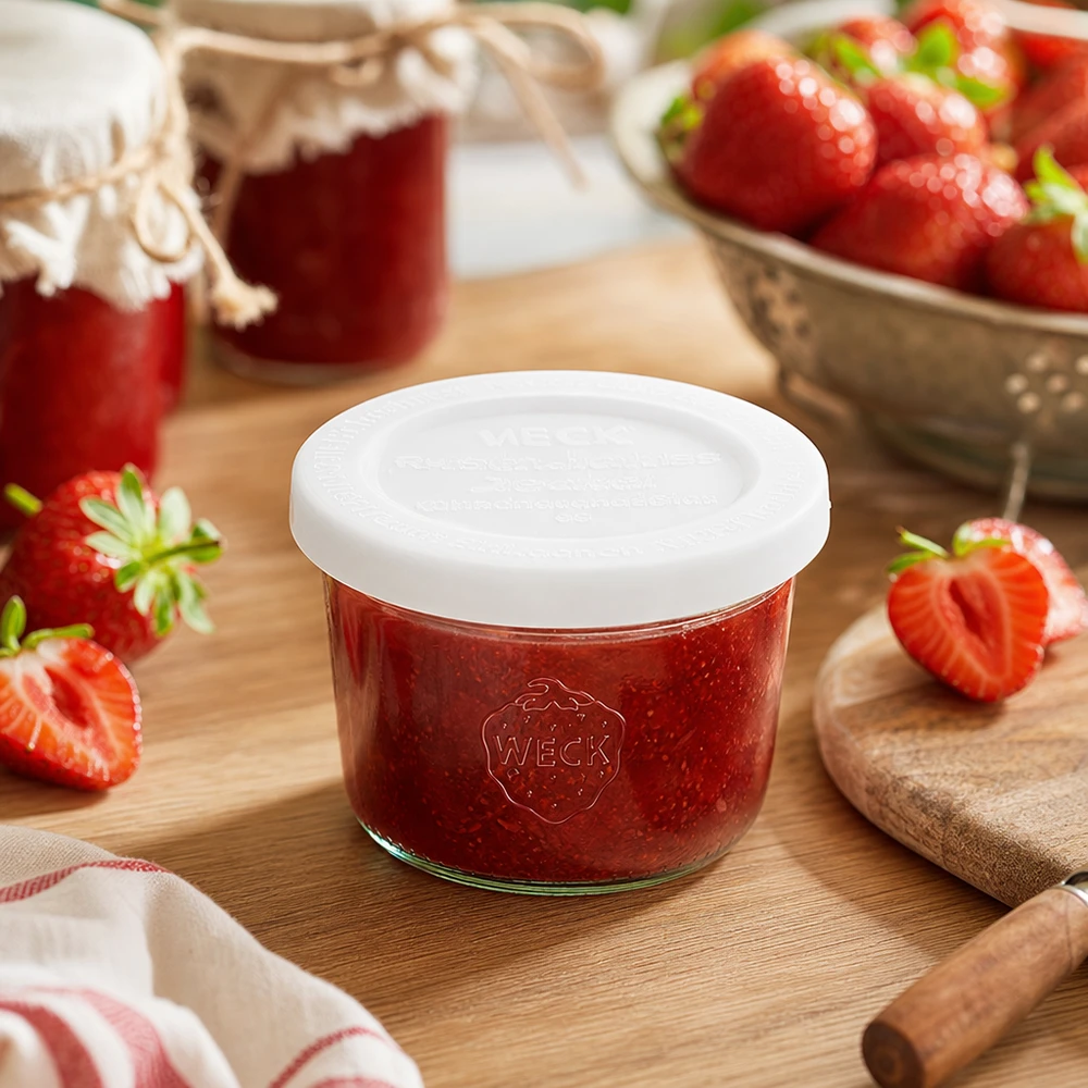 Bocal en verre de 80 ml avec couvercle hermétique WECK RR60 WECK 80ml Sturzglas RR60 mit Erdbeermarmelade gefüllt auf Holzbrett umgeben von frischen Erdbeeren und Marmeladengläsern