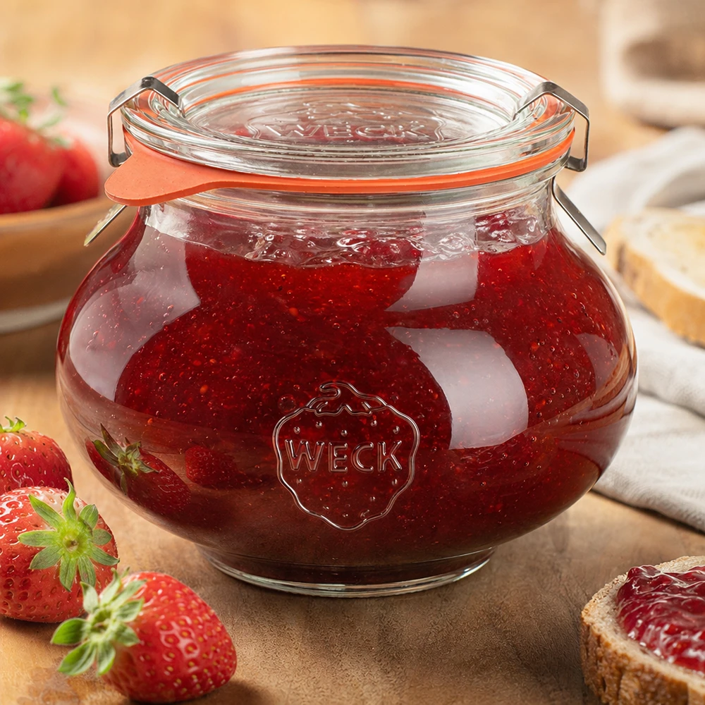 Vaso decorativo da 560 ml completo WECK RR80 Vaso decorativo WECK da 560 ml riempito di marmellata di fragole fatta in casa, con coperchio chiuso, circondato da frutta e verdura fresca.