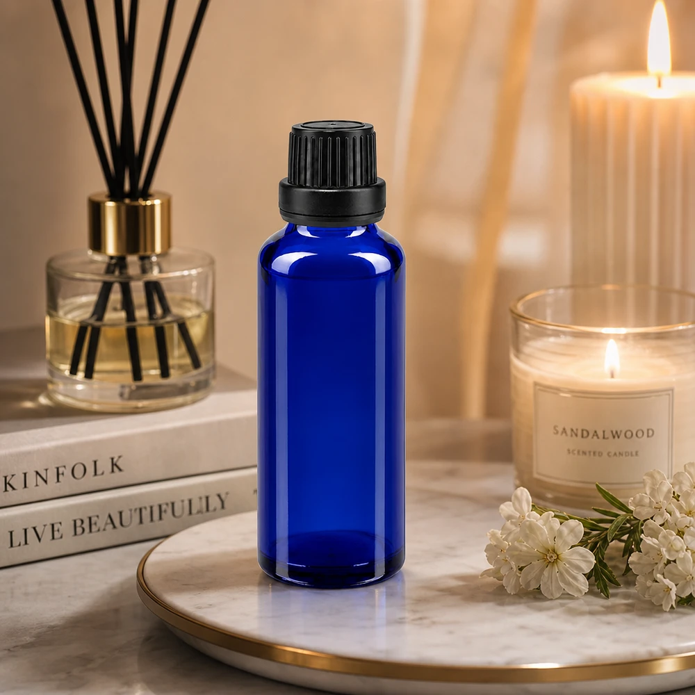 Flacon en verre bleu de 30 ml muni d'un bouchon OV noir, posé sur un plateau en marbre à côté d'une bougie au bois de santal et d'un diffuseur