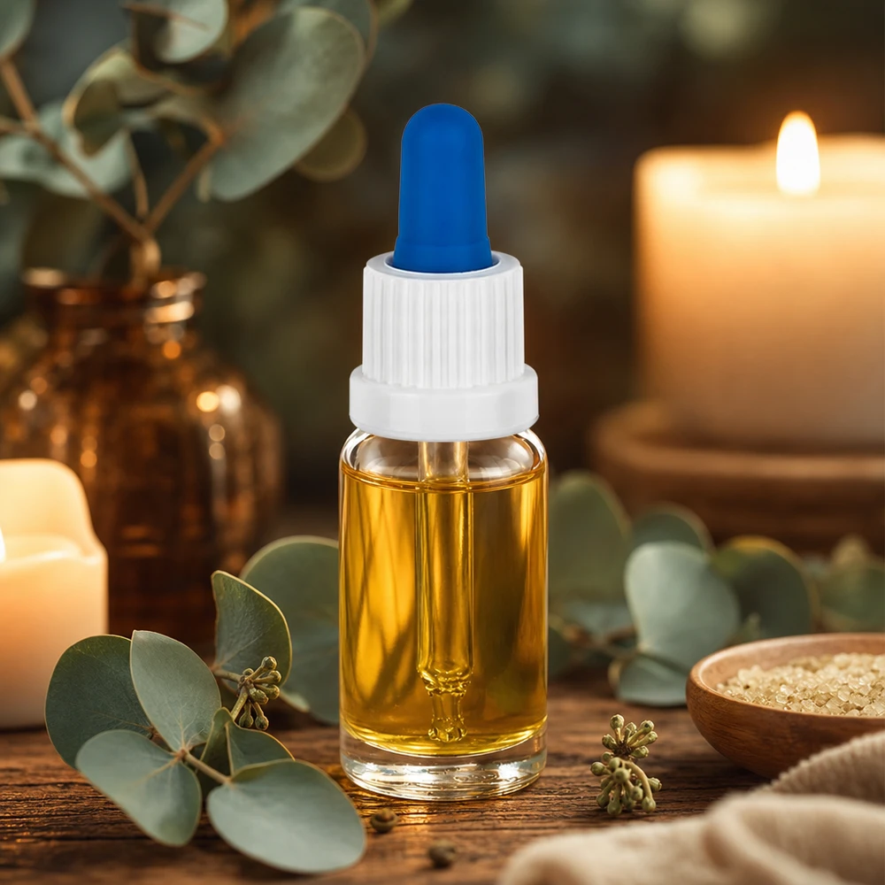 Flacon à pipette 10ml blanc/bleu OV ClearL. UT18/10 Petit flacon pipette de 10 ml contenant de l'huile dorée, muni d'un bouchon blanc et d'une bille en caoutchouc bleue, posé sur une table en bois