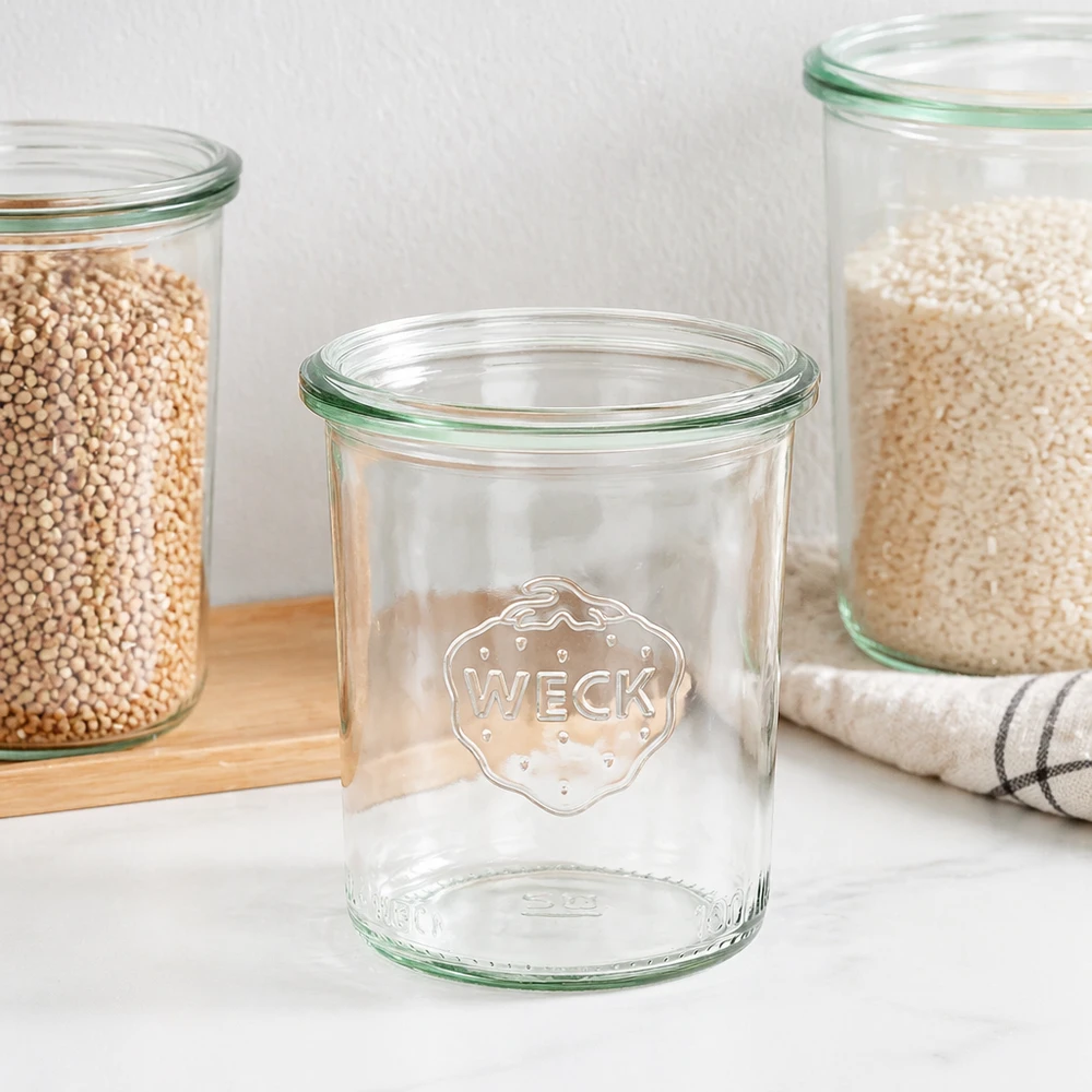 Barattolo da 160ml WECK RR60 WECK 160ml RR60 mason jar con bordo verde e logo, mason jar vuoto accanto a barattoli pieni su tavola di legno