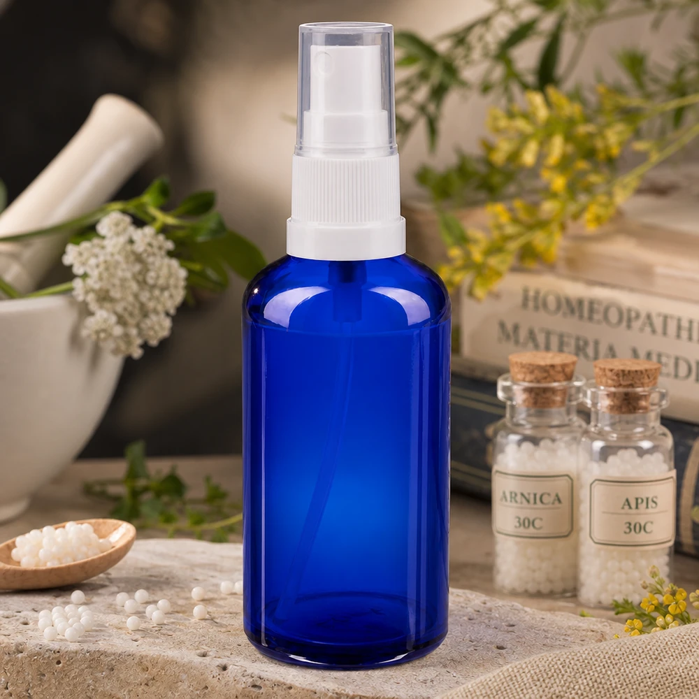 Blaues 50ml Apothekerglas mit weißem Sprühkopf neben Mörser und Heilpflanzen