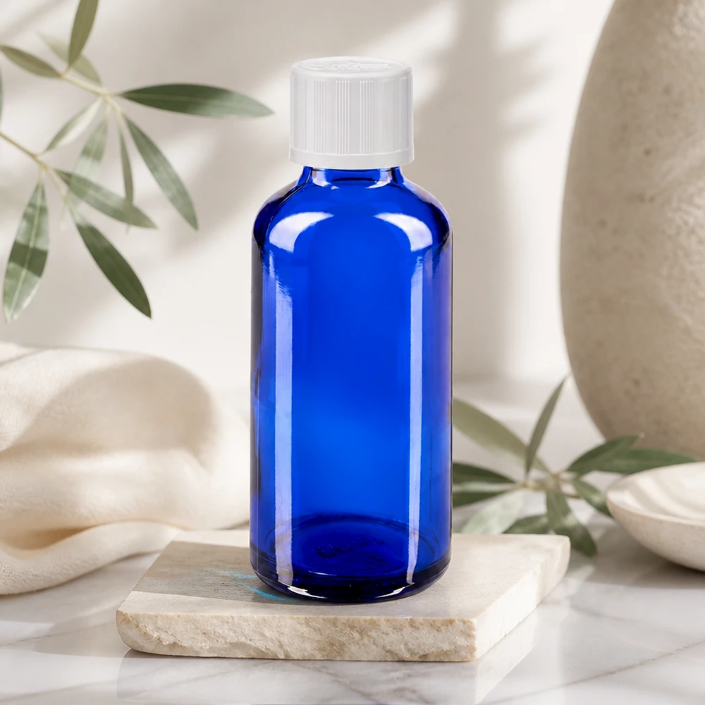Bouteille en verre bleue de 50 ml avec un bouchon à vis blanc, posée sur une pierre de marbre dans un décor naturel clair